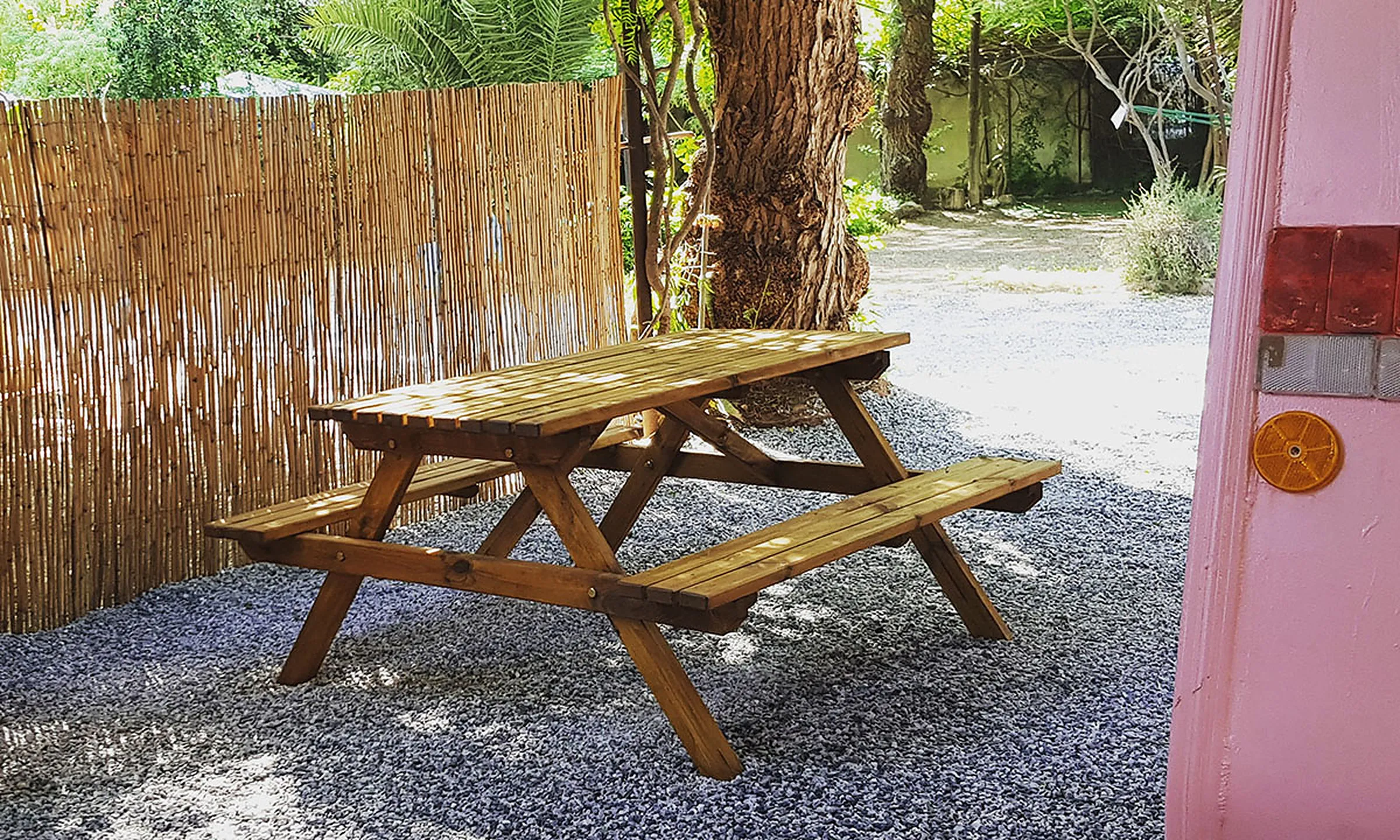 Table de pique-nique en bois à côté d'une caravane, avec canisse et ombre