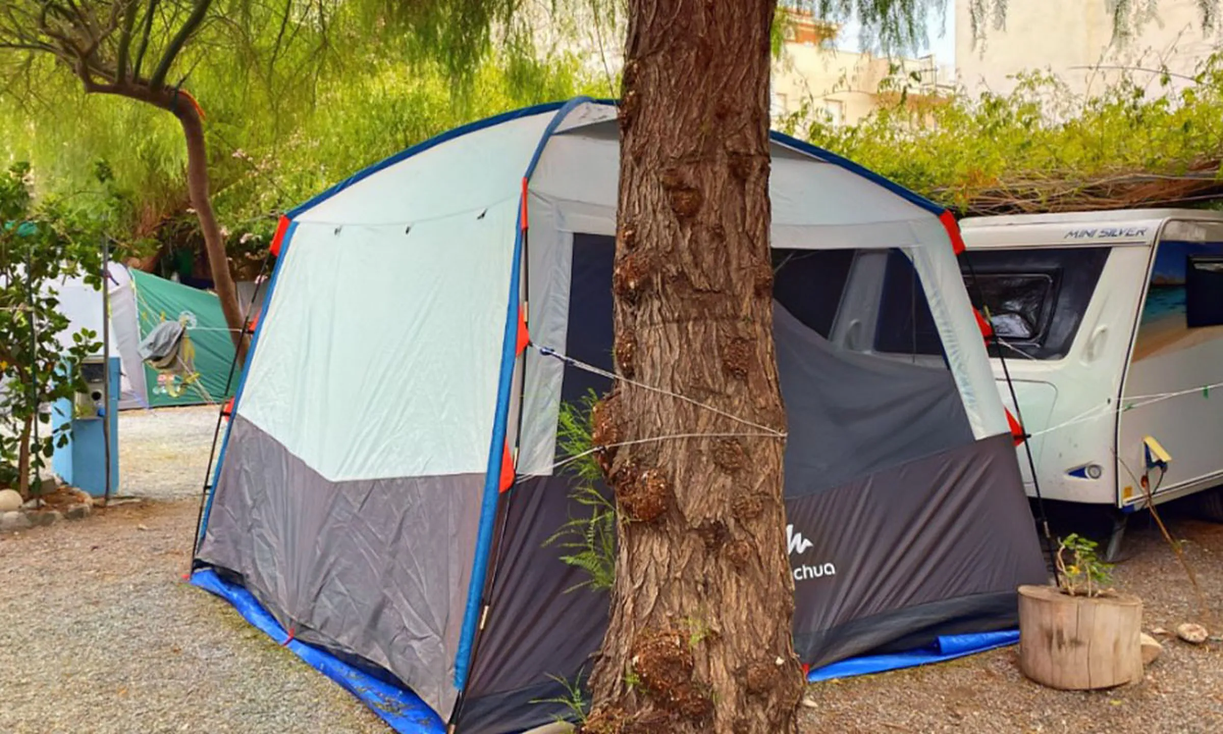 Tente familiale montée sur un emplacement ombragé à côté d'une caravane