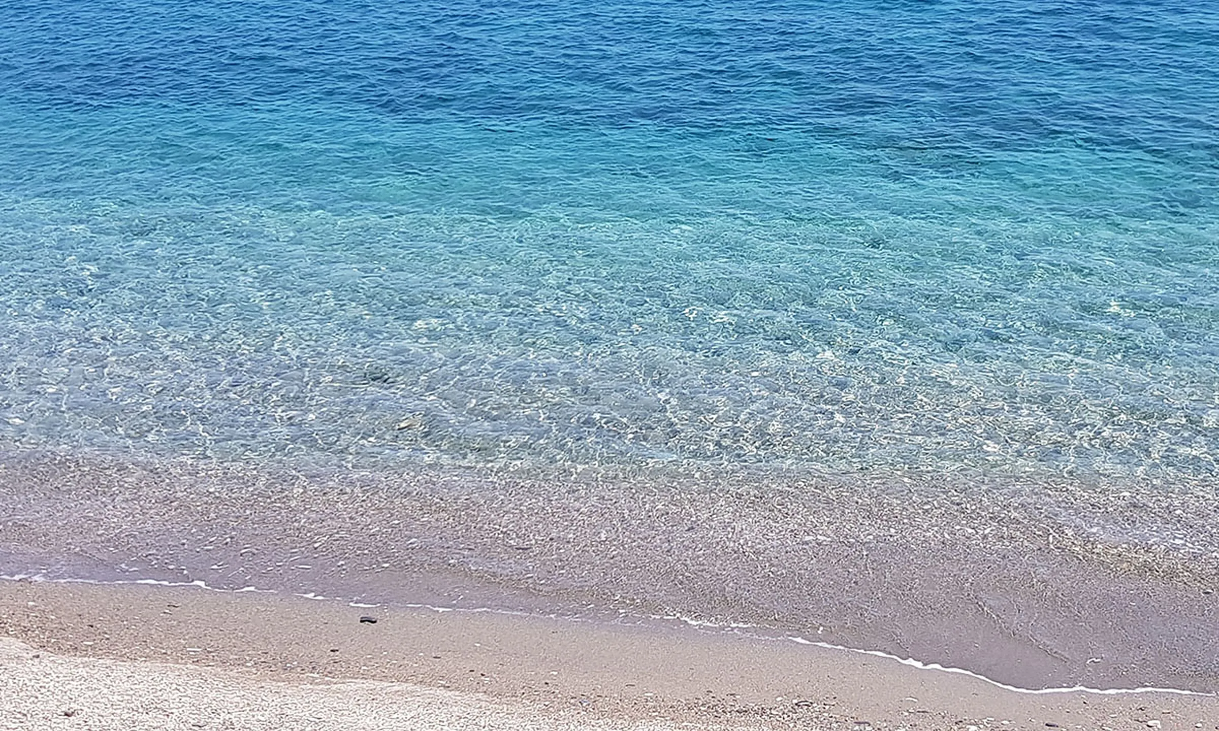 Rivage de la plage de Castell de Ferro, avec des eaux turquoise et cristallines sur du sable et des petits galets